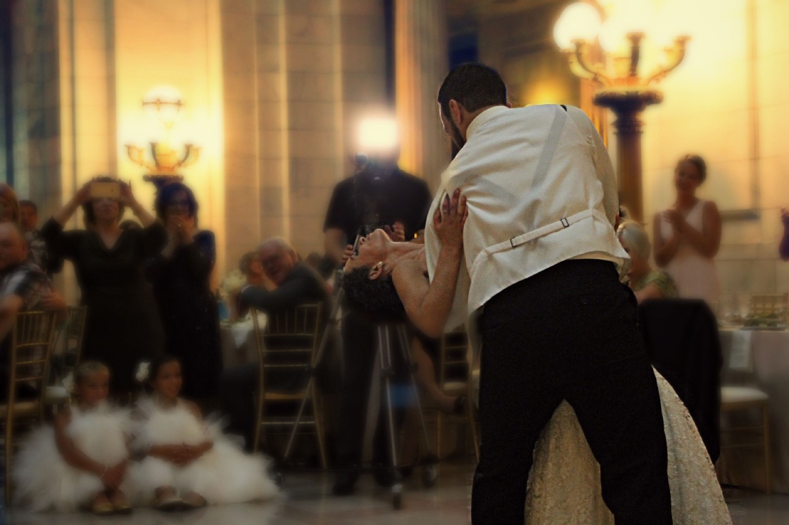 Los novios bailando el primer baile en un salón con luz cálida, rodeados de invitados que aplauden