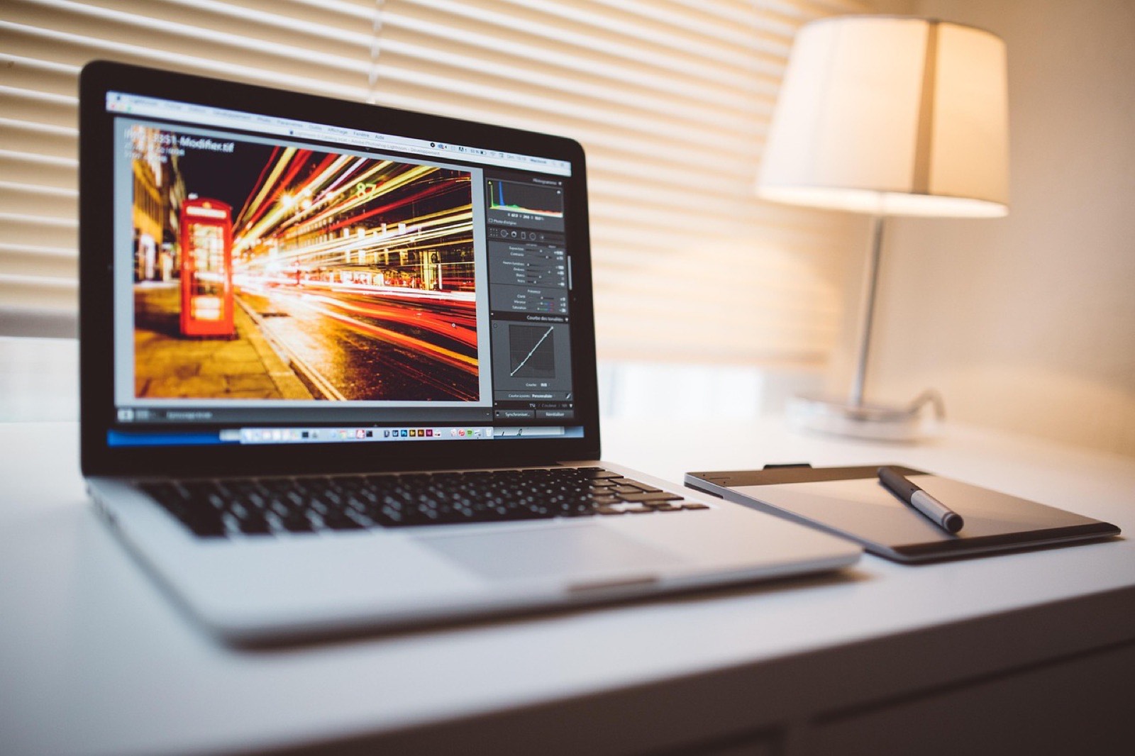 Laptop sobre un escritorio blanco con una fotografía abierta en un editor de imagen, junto a una tableta gráfica y su lápiz