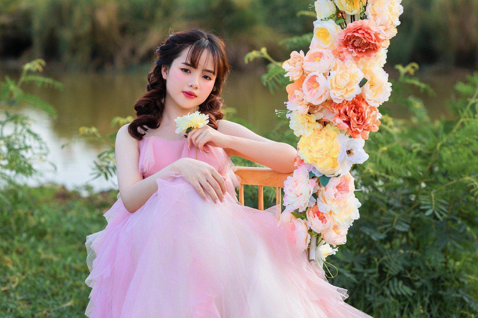 Chica con vestido rosa de tul sentada en un columpio adornado con flores, en un jardín con luz de atardecer